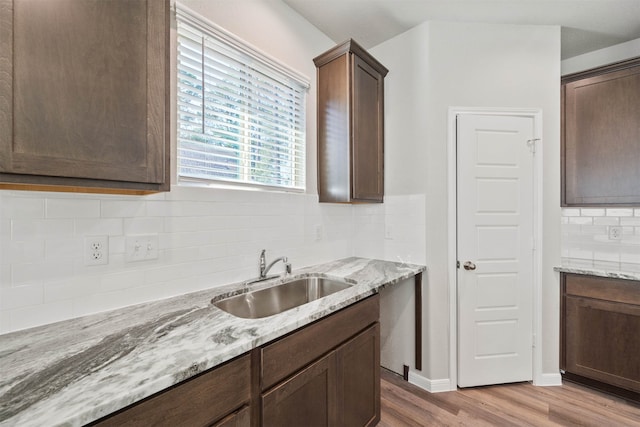 kitchen featuring backsplash, light stone countertops, light hardwood / wood-style flooring, dark brown cabinetry, and sink