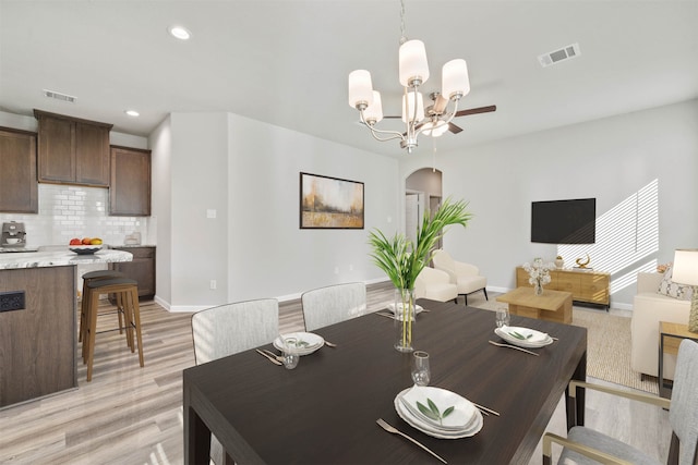 dining space with ceiling fan with notable chandelier and light hardwood / wood-style floors