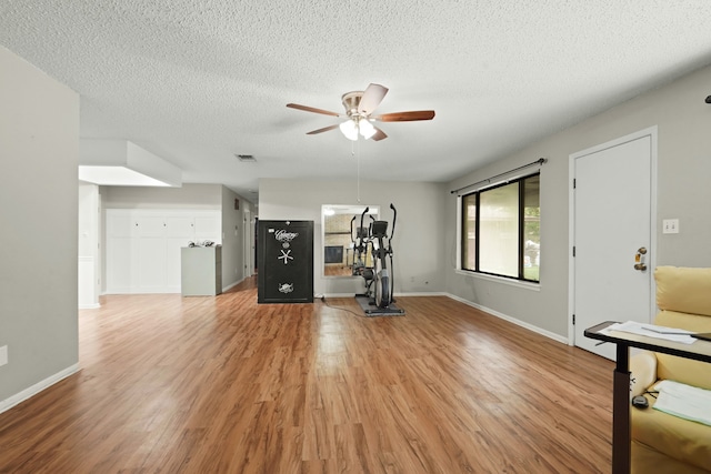 workout area with ceiling fan, a textured ceiling, and light hardwood / wood-style flooring