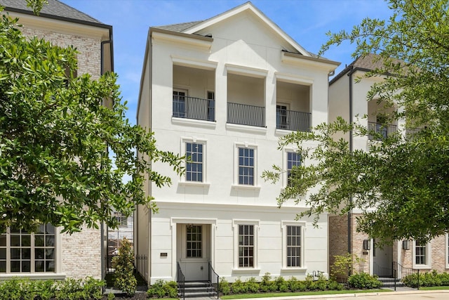 greek revival inspired property featuring a balcony, entry steps, and stucco siding
