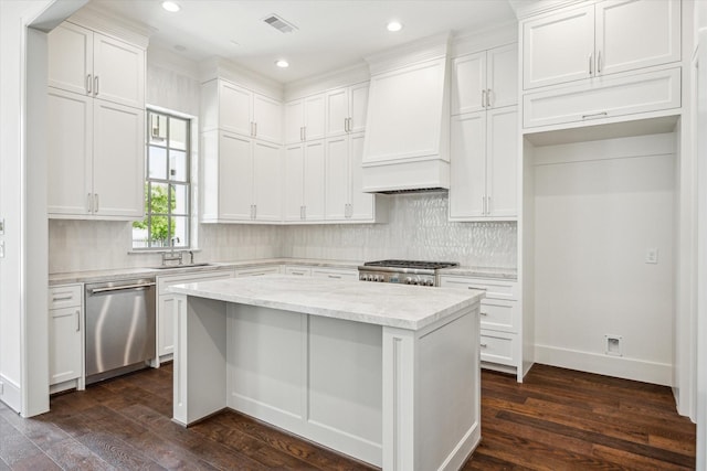 kitchen featuring appliances with stainless steel finishes, premium range hood, a sink, tasteful backsplash, and white cabinets