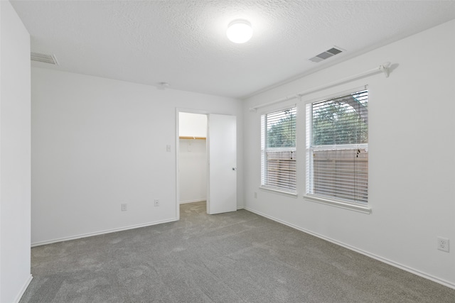 unfurnished bedroom with carpet floors, a textured ceiling, a walk in closet, and a closet