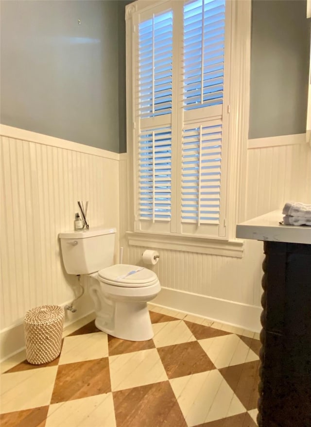 bathroom featuring toilet, a decorative wall, and a wainscoted wall