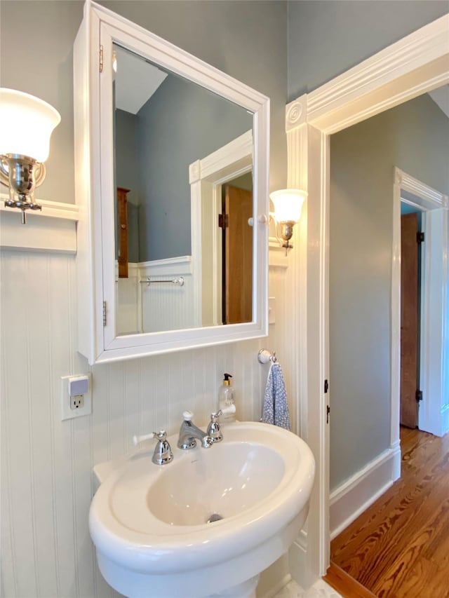 bathroom featuring a sink, a decorative wall, wainscoting, and wood finished floors