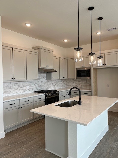 kitchen with sink, hanging light fixtures, light stone countertops, gas stove, and built in microwave