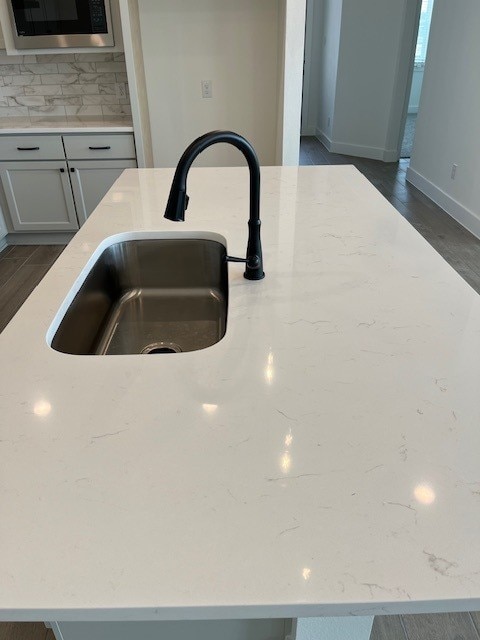 interior details with tasteful backsplash, sink, stainless steel microwave, and dark hardwood / wood-style flooring