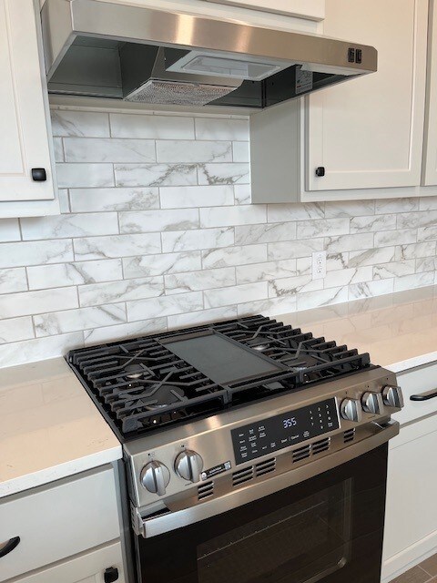 kitchen with tasteful backsplash, white cabinetry, stainless steel gas range, and range hood