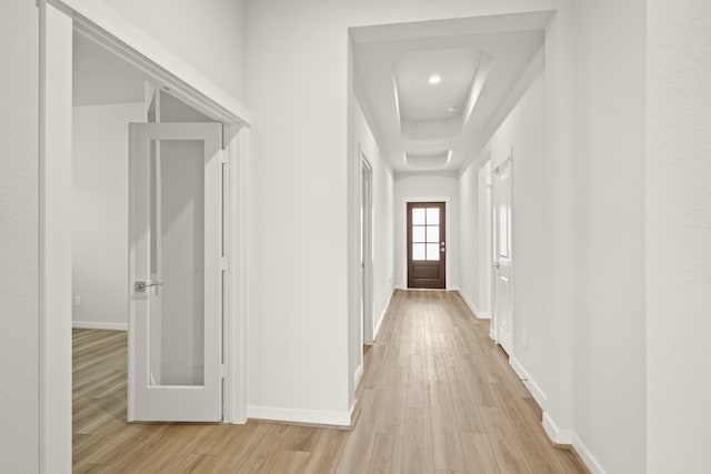 hall with light hardwood / wood-style floors and a raised ceiling