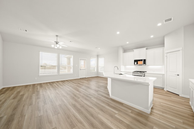 kitchen with stainless steel gas stove, an island with sink, sink, white cabinets, and light hardwood / wood-style floors