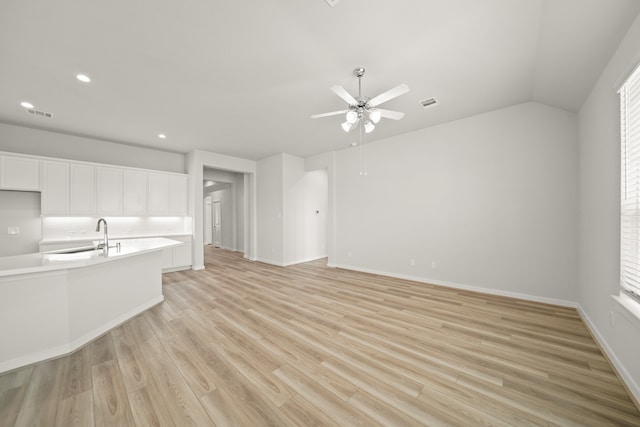 unfurnished living room with ceiling fan, lofted ceiling, sink, and light wood-type flooring