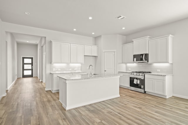 kitchen with decorative backsplash, white cabinetry, stainless steel appliances, and light hardwood / wood-style floors