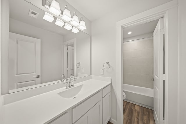 full bathroom featuring vanity, tiled shower / bath combo, hardwood / wood-style flooring, and toilet