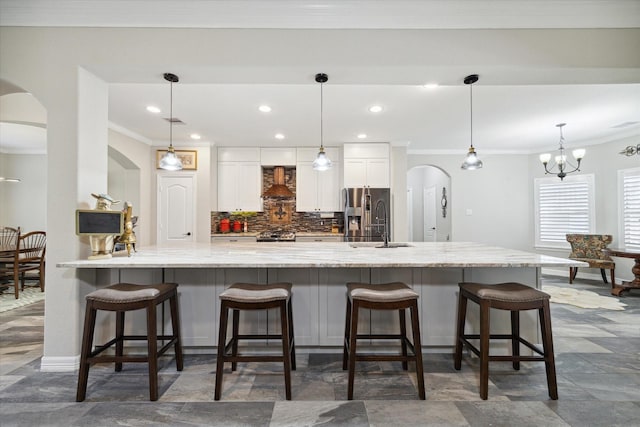 kitchen featuring a kitchen breakfast bar, pendant lighting, white cabinets, and wall chimney range hood