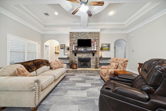 living room featuring ceiling fan, crown molding, a stone fireplace, and coffered ceiling