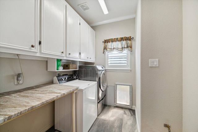 laundry area featuring washing machine and dryer, cabinets, and light wood-type flooring