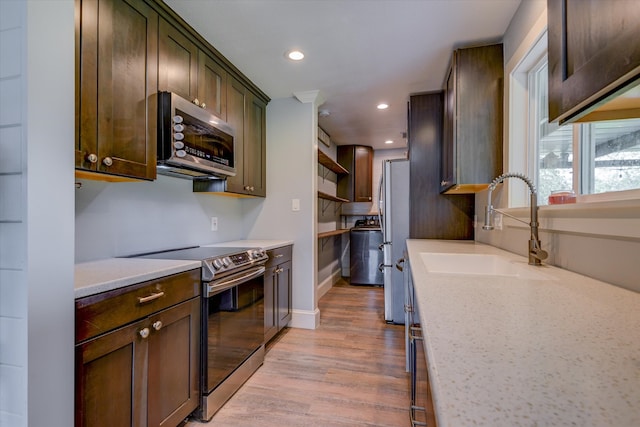 kitchen with appliances with stainless steel finishes, light stone countertops, light wood-type flooring, and sink