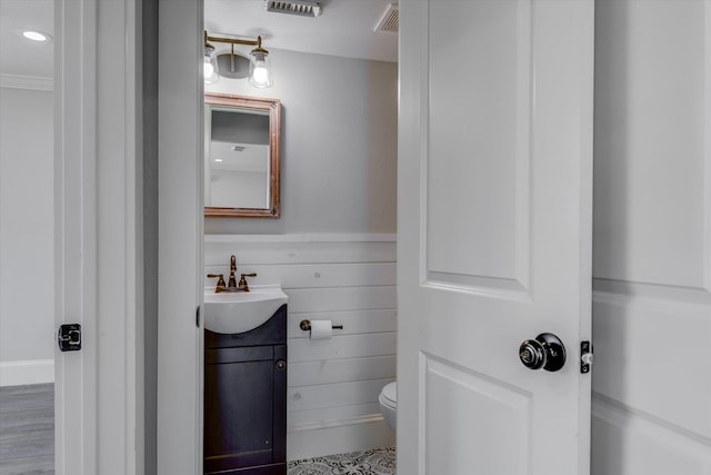 bathroom featuring wooden walls, hardwood / wood-style flooring, vanity, and toilet