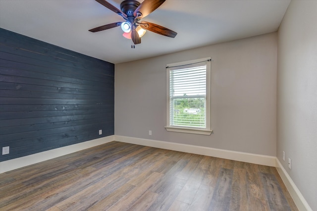 unfurnished room featuring ceiling fan, wood walls, and dark hardwood / wood-style flooring