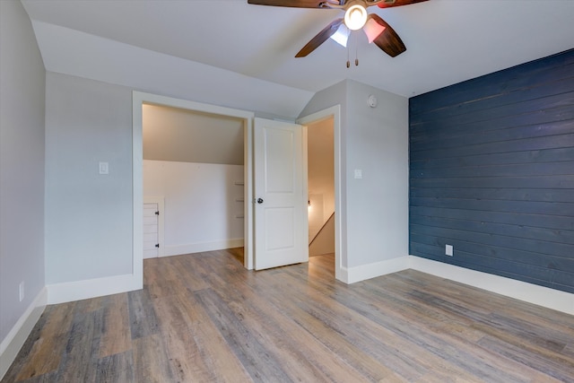 unfurnished bedroom featuring wood walls, a closet, lofted ceiling, ceiling fan, and hardwood / wood-style flooring