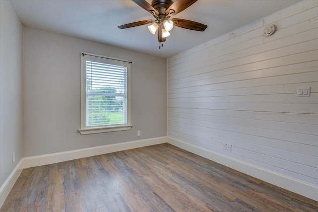 spare room with ceiling fan, hardwood / wood-style flooring, and wood walls