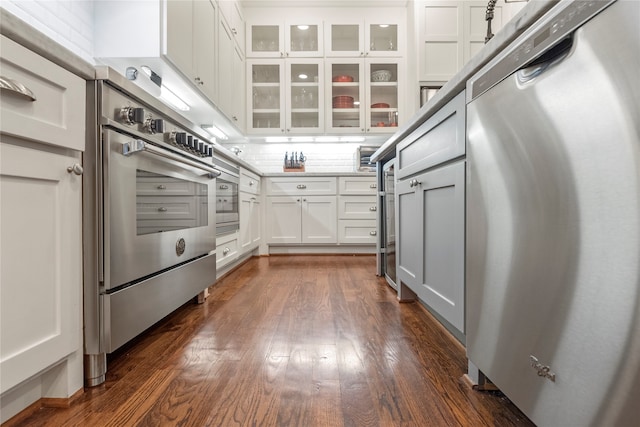 kitchen with dark hardwood / wood-style floors, decorative backsplash, white cabinetry, and stainless steel appliances