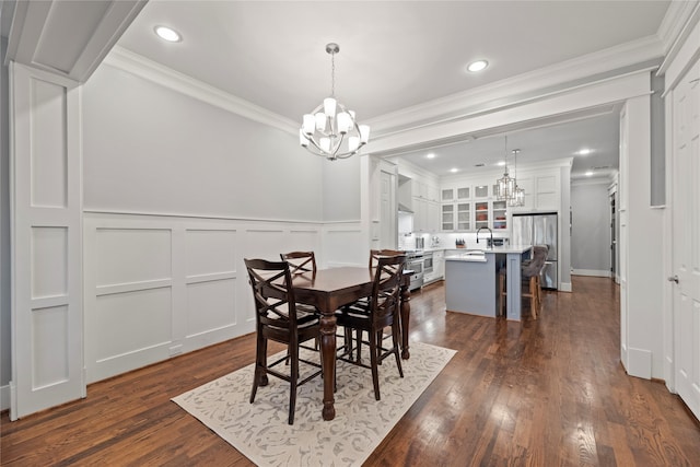 dining space featuring dark wood-type flooring, crown molding, an inviting chandelier, and sink