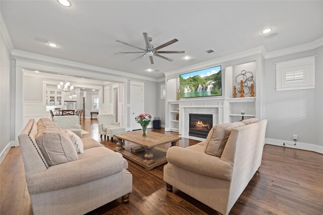 living room with dark wood-type flooring, ceiling fan with notable chandelier, ornamental molding, and a premium fireplace