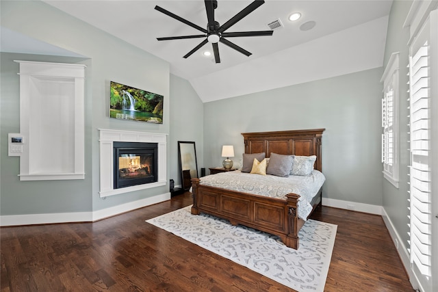 bedroom featuring dark wood-type flooring, a multi sided fireplace, vaulted ceiling, and ceiling fan