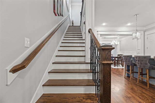 stairway with wood-type flooring, ornamental molding, and a notable chandelier