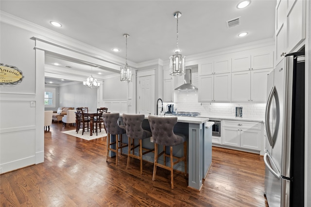 kitchen with a kitchen island with sink, stainless steel appliances, white cabinets, dark wood-type flooring, and wall chimney range hood