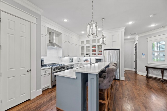 kitchen with white cabinets, an island with sink, wall chimney exhaust hood, stainless steel appliances, and dark hardwood / wood-style flooring