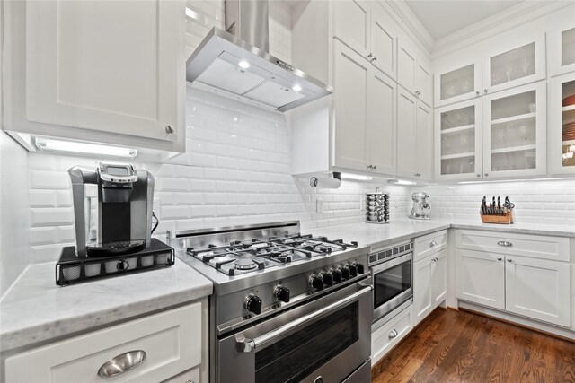 kitchen with light stone counters, dark wood-type flooring, wall chimney range hood, white cabinetry, and appliances with stainless steel finishes