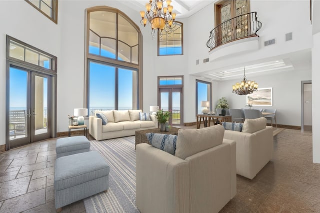 living room featuring a towering ceiling, a tray ceiling, french doors, ornamental molding, and a chandelier