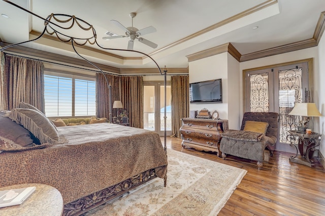 bedroom with light hardwood / wood-style floors, crown molding, a tray ceiling, ceiling fan, and french doors