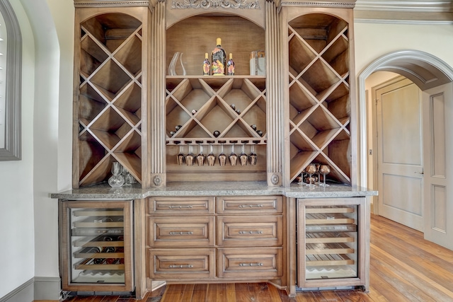 wine cellar with ornamental molding, beverage cooler, and wood-type flooring