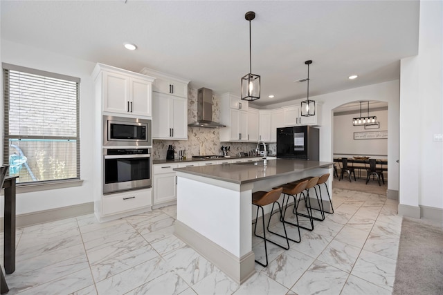 kitchen with wall chimney exhaust hood, sink, an island with sink, white cabinets, and appliances with stainless steel finishes