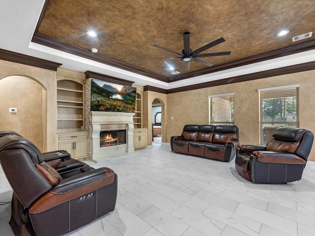 living room with crown molding, a tray ceiling, ceiling fan, built in features, and a premium fireplace