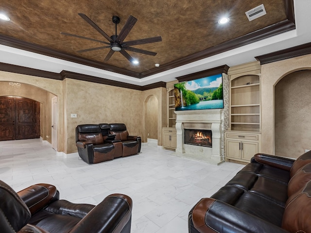 living room with built in shelves, a premium fireplace, ornamental molding, and ceiling fan