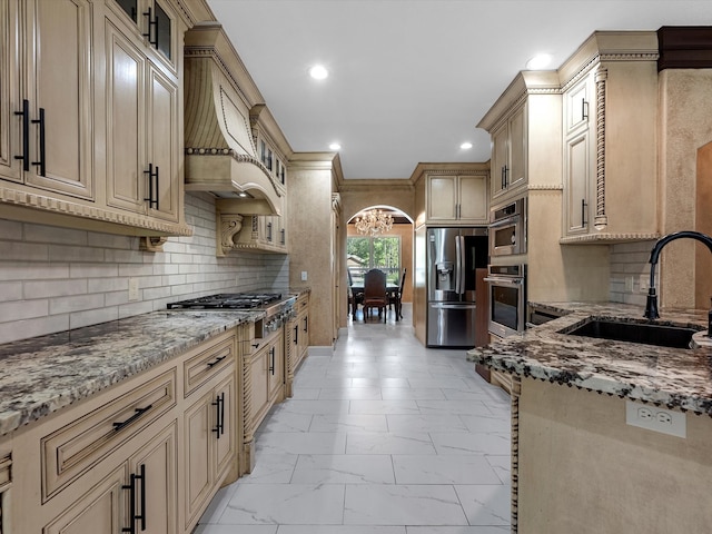 kitchen with light stone counters, tasteful backsplash, stainless steel appliances, premium range hood, and sink