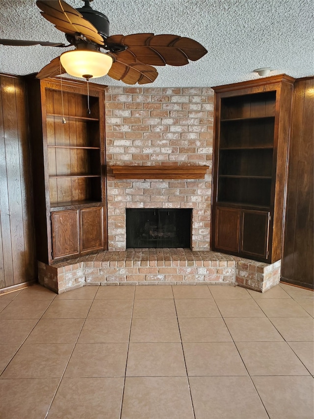 unfurnished living room with wooden walls, ceiling fan, a fireplace, and a textured ceiling