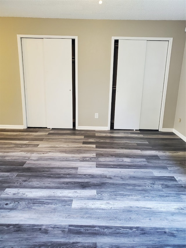 unfurnished bedroom featuring two closets and dark wood-type flooring