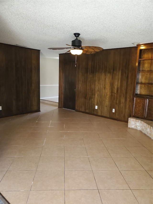 unfurnished living room featuring ceiling fan, a textured ceiling, wooden walls, and light tile patterned floors