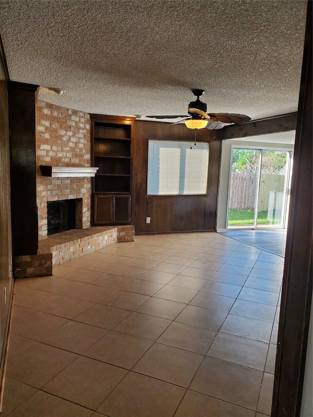 unfurnished living room featuring a brick fireplace, light tile patterned floors, a textured ceiling, ceiling fan, and built in shelves