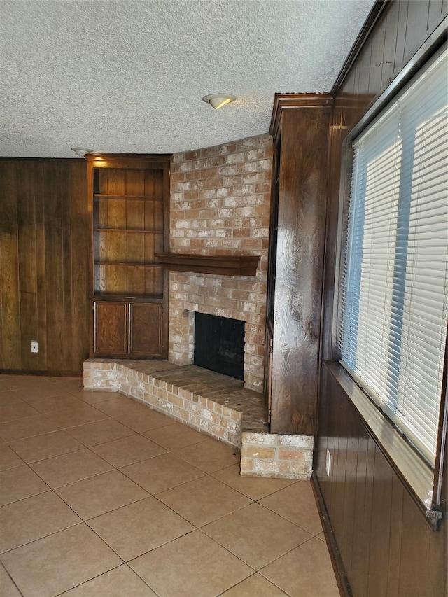 unfurnished living room with a brick fireplace, a textured ceiling, wood walls, and light tile patterned floors