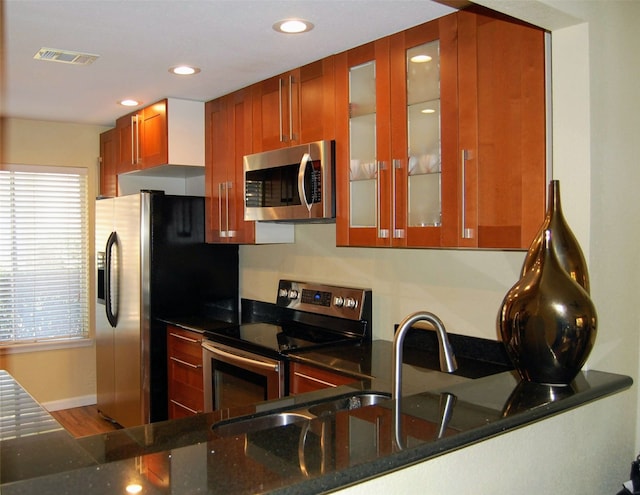 kitchen featuring wood-type flooring, appliances with stainless steel finishes, kitchen peninsula, and dark stone countertops