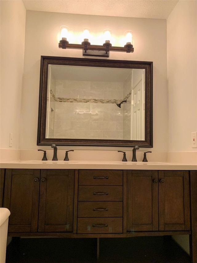 bathroom featuring a textured ceiling, a tile shower, vanity, and toilet