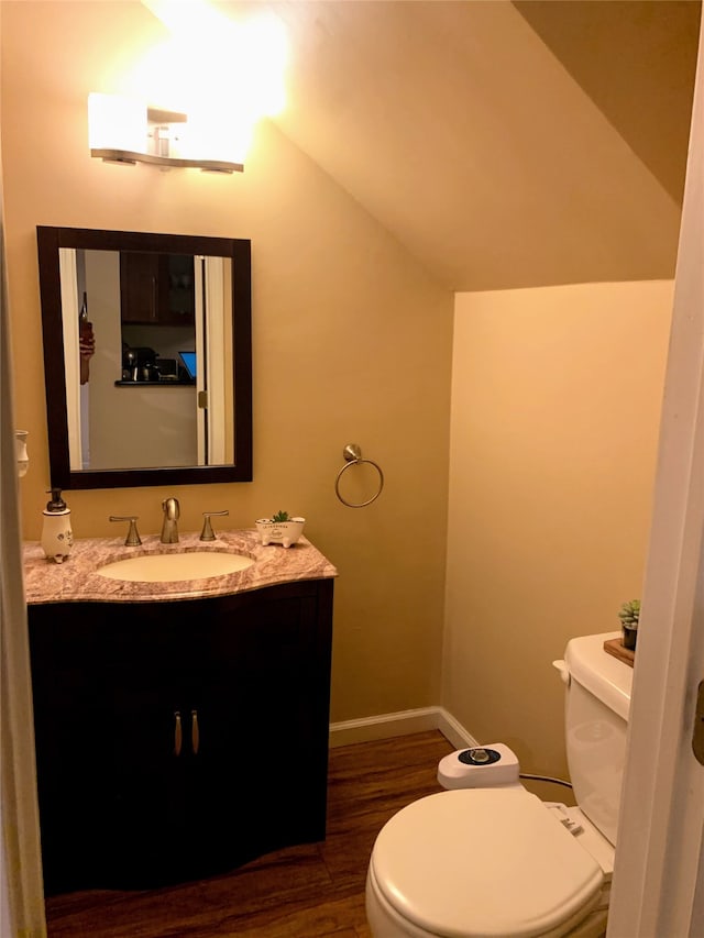 bathroom featuring wood-type flooring, vanity, lofted ceiling, and toilet