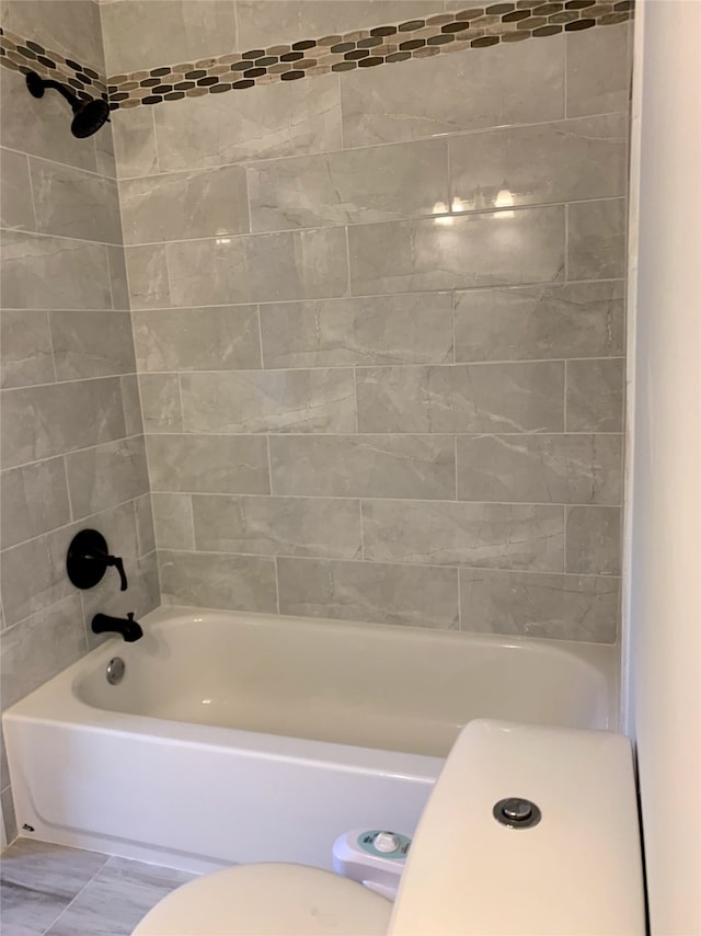 bathroom featuring tiled shower / bath combo and toilet