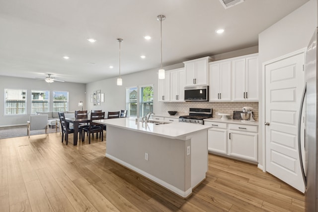 kitchen with a kitchen island with sink, pendant lighting, stainless steel appliances, and light hardwood / wood-style flooring