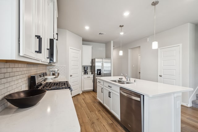 kitchen featuring a kitchen island with sink, sink, hanging light fixtures, light wood-type flooring, and stainless steel appliances